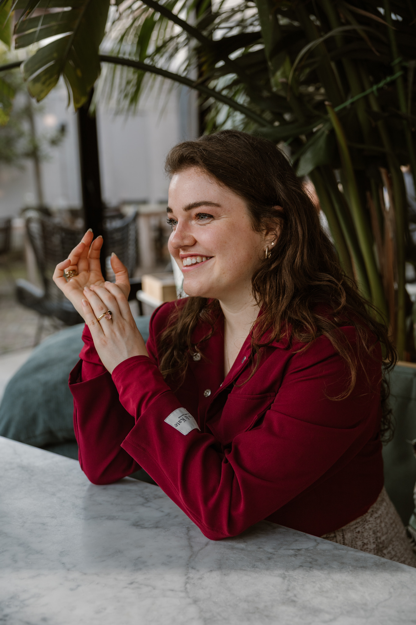 Mirjam tijdens branding shoot in rode blazer aan tafel met planten op achtergrond